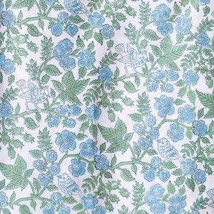 May include: White fabric with a repeating pattern of light blue flowers, green leaves, and perched birds. The design features detailed illustrations of birds and floral elements, creating a nature-inspired aesthetic. The fabric has a soft, flowing appearance.
