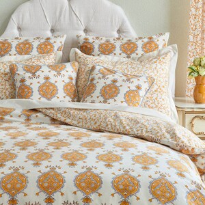 May include: A white bed with a white headboard and a white and yellow patterned duvet cover. The duvet cover has a paisley design with yellow and blue accents. There are several pillows on the bed, all with the same paisley design.