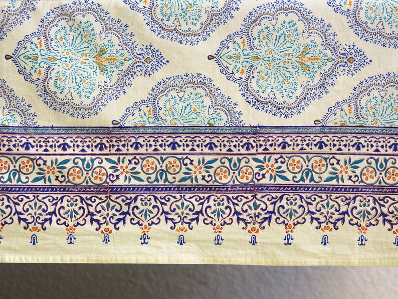 Puede incluir: Textil color crema con un patr&oacute;n repetitivo de medallones florales turquesa y azul marino. Un borde azul marino con dise&ntilde;os florales y de desplazamiento recorre la parte inferior. Probablemente un mantel o tela.