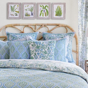 May include: A bedroom scene featuring a bed with a woven headboard, adorned with blue and green patterned bedding and pillows. Above the bed, four framed botanical prints hang on the wall. Matching curtains and a bedside lamp complete the coordinated decor.