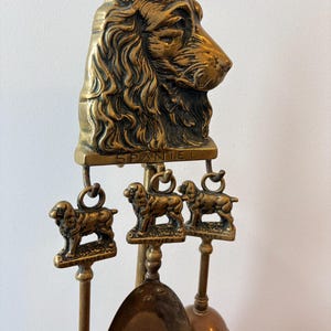 Pode incluir: Um conjunto de ferramentas para lareira em latão com uma grande escultura de cabeça de spaniel no topo. Três figuras menores de spaniel estão suspensas por ganchos abaixo da cabeça. Cada figura pequena tem uma base com a palavra SPANIEL.
