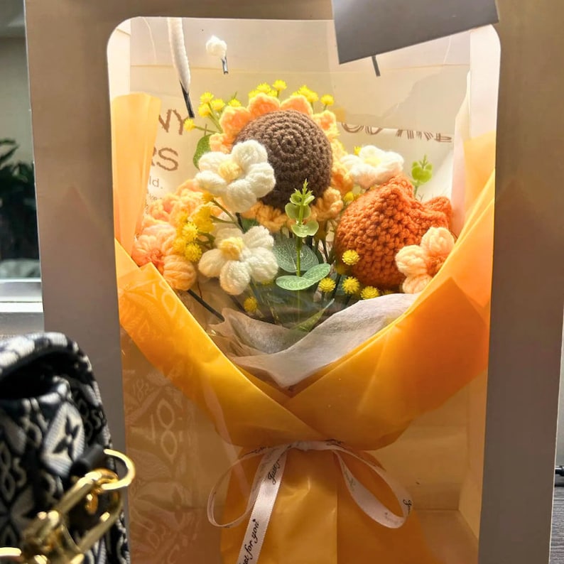 May include: A crocheted bouquet of sunflowers and other flowers in a yellow paper wrapping with a white ribbon that says "Just for you".
