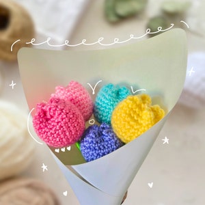 May include: A bouquet of five crocheted tulips in a white paper cone. The tulips are pink, blue, yellow, and purple.