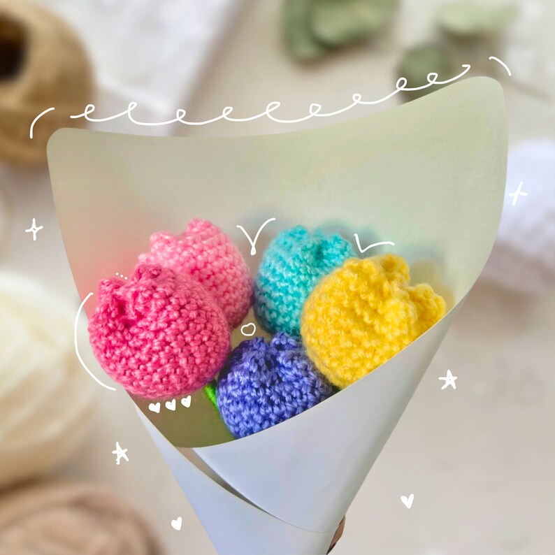 May include: A bouquet of five crocheted tulips in a white paper cone. The tulips are pink, blue, yellow, and purple.