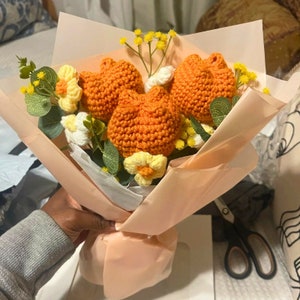 May include: A bouquet of crocheted orange flowers with white and yellow flower accents wrapped in peach-coloured tissue paper.