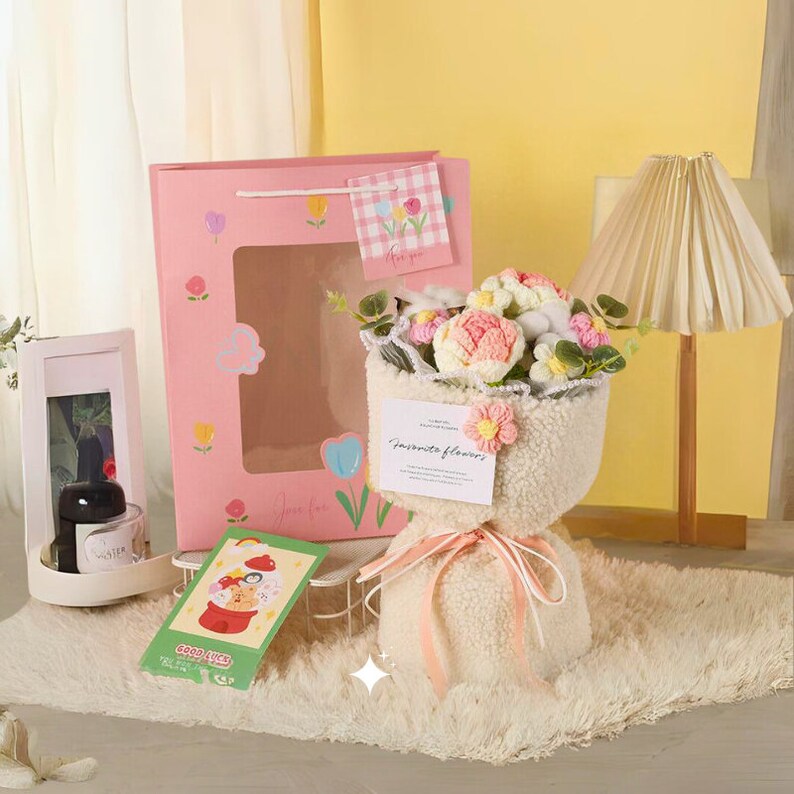 May include: A white faux fur bouquet of pink and white crocheted flowers with a pink ribbon and a tag that says "favorite flowers". The bouquet is sitting on a white fluffy rug. There is a pink gift bag with a white and pink checkered tag that says "for you" in the background.