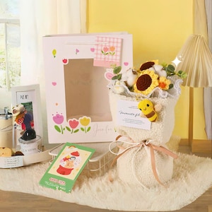 May include: A white gift bag with a window showing a crocheted sunflower bouquet with a bee charm. The bag has a pink and white gingham tag that says "Just for you".