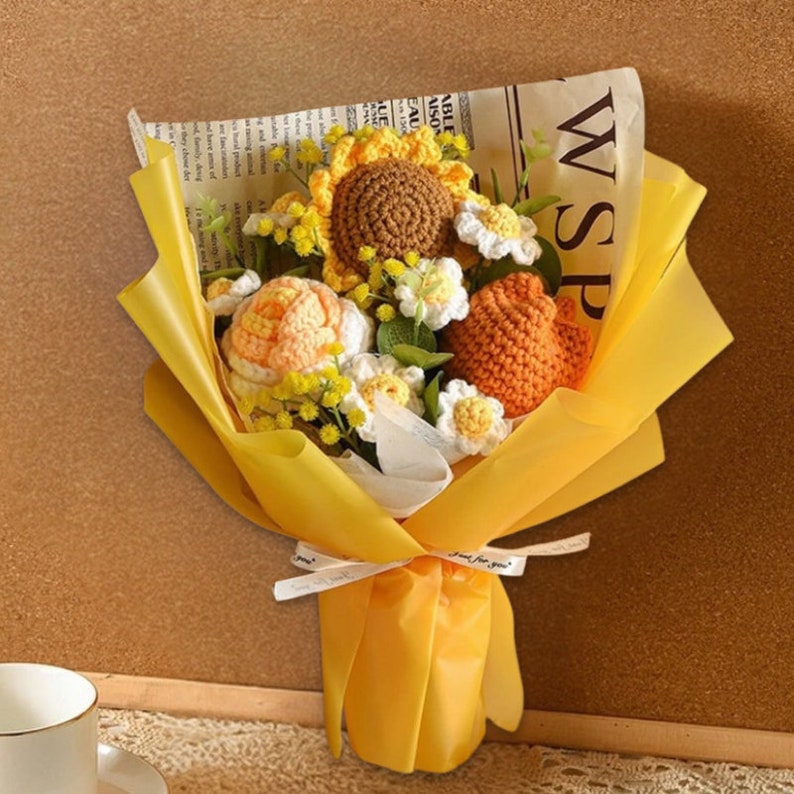 May include: A yellow paper bouquet featuring crocheted sunflowers, daisies, and roses. The bouquet is tied with a white ribbon and has the words "Just for you" printed on it.