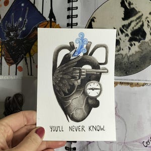 Puede incluir: Una ilustraci&oacute;n en blanco y negro de un coraz&oacute;n con un p&aacute;jaro posado en la parte superior, sosteniendo una pistola. El coraz&oacute;n tiene una esfera de reloj y un remolino azul que sale de &eacute;l. El texto "You'll never know." est&aacute; escrito debajo del coraz&oacute;n.