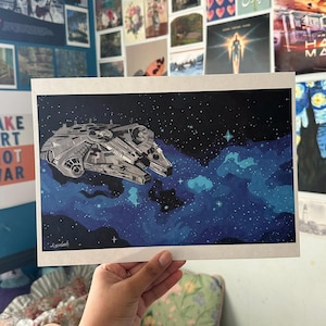 May include: A rectangular art print featuring a detailed illustration of a grey starship flying through deep space. The background consists of a dark blue and black nebula filled with scattered white stars and bright light points.