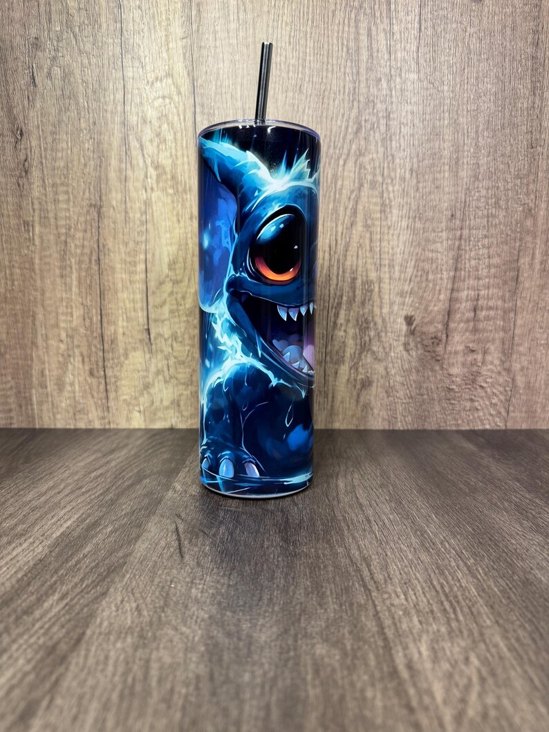Pu&ograve; includere: Un bicchiere in acciaio inossidabile con un'illustrazione di un personaggio alieno blu. Il design presenta un personaggio con grandi occhi e denti affilati, con accenti blu elettrico e una cannuccia nera. Il bicchiere &egrave; cilindrico.