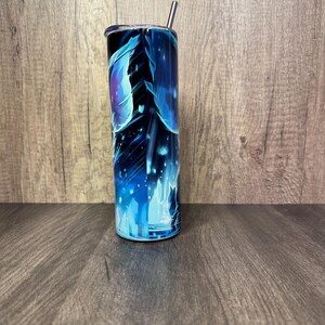 Pu&ograve; includere: Un bicchiere alto e cilindrico con un vivace design astratto blu e viola. Il bicchiere ha una cannuccia argentata e un coperchio nero. Il design presenta forme fluide e un effetto stellato.