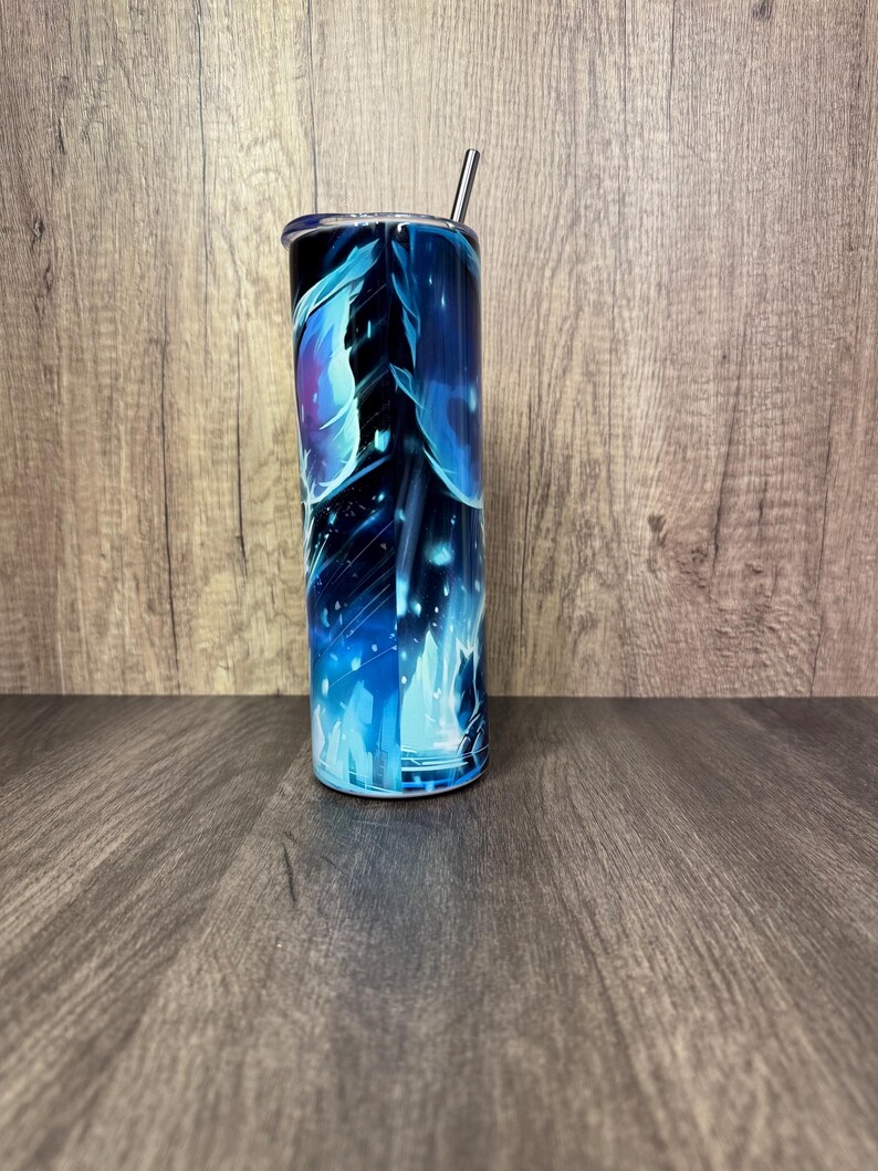 Pu&ograve; includere: Un bicchiere alto e cilindrico con un vivace design astratto blu e viola. Il bicchiere ha una cannuccia argentata e un coperchio nero. Il design presenta forme fluide e un effetto stellato.