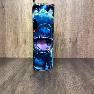 Pu&ograve; includere: Un bicchiere blu con un design di personaggio dei cartoni animati, che mostra un ampio sorriso e denti affilati. Il design utilizza sfumature di blu e viola, con una cannuccia e un coperchio neri. Il bicchiere cilindrico &egrave; probabilmente in acciaio inossidabile.