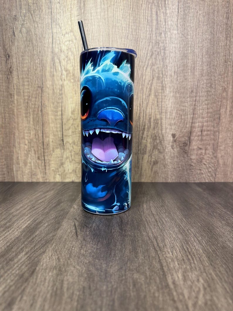 Pu&ograve; includere: Un bicchiere blu con un design di personaggio dei cartoni animati, che mostra un ampio sorriso e denti affilati. Il design utilizza sfumature di blu e viola, con una cannuccia e un coperchio neri. Il bicchiere cilindrico &egrave; probabilmente in acciaio inossidabile.