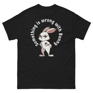Op de afbeelding: Zwart T-shirt met een witte cirkelvormige afbeelding met een cartoonkonijn met de tekst "Something is wrong with Bunny".