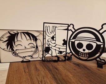 May include: Black and white anime-style cutouts of characters and a skull logo. The first cutout features a smiling character with a straw hat. The second cutout shows a character with a hat. The third cutout is a skull with a hat and crossbones.