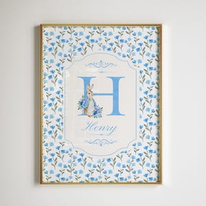 Peut inclure: Une impression de crèche personnalisée bleue et blanche avec un motif floral bleu, une lettre H bleue, une illustration de lapin et le nom Henry.