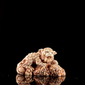 May include: A small, detailed, beige ceramic sculpture of a lion sitting on a bed of flowers. The sculpture is on a black background.