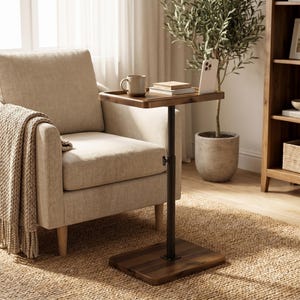 May include: A dark wood C-shaped side table with a black metal support pole and adjustable height knob. The rectangular tabletop holds a ceramic mug, a small stack of books, and a white smartphone. The base is a flat, rectangular dark wood piece.