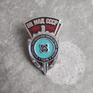 Peut inclure: Un badge vintage de l'ère soviétique avec du texte cyrillique et un motif de bouclier. Le badge présente une palette de couleurs rouge et argent avec un emblème bleu central. Le texte comprend "BB МВД СССР" et d'autres phrases cyrilliques.