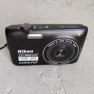 May include: A black Nikon Coolpix S4150 digital camera featuring a 5x wide optical zoom lens, a 14.0 megapixel sensor, and a touch screen interface. The top panel includes a shutter button, a zoom toggle, and an on/off power button.