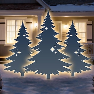 Peut inclure: Trois découpes d'arbres de Noël stylisées, bleu foncé et éclairées, avec des étoiles, se dressent dans un jardin enneigé. Les arbres sont devant une maison éclairée, créant une scène de vacances festive.