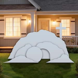 May include: A white, layered cutout of an empty tomb with a cross, set in front of a house with a green lawn. The tomb has a large, round stone at the entrance. The house has a porch and windows.