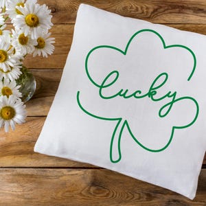 May include: White pillow with a green outline of a four-leaf clover and the word "lucky" written in cursive.