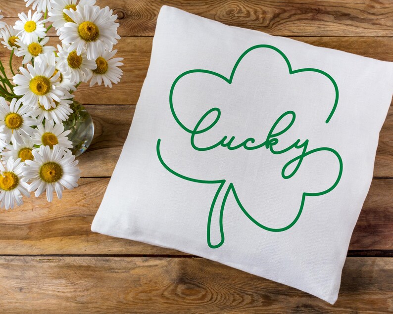 May include: White pillow with a green outline of a four-leaf clover and the word "lucky" written in cursive.