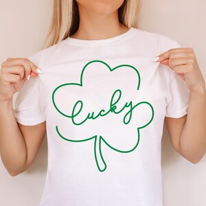 May include: White t-shirt with a green outline of a four-leaf clover and the word "lucky" written inside.