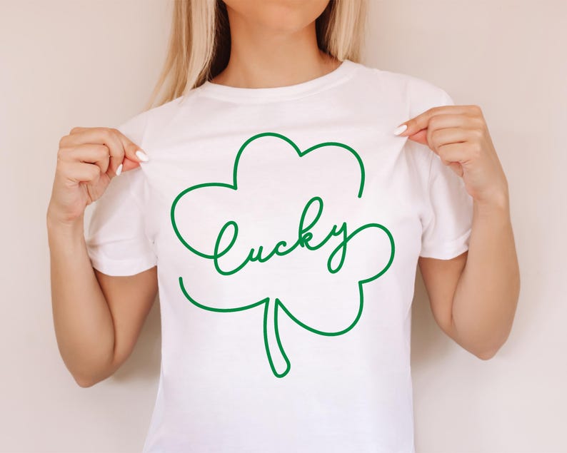 May include: White t-shirt with a green outline of a four-leaf clover and the word "lucky" written inside.