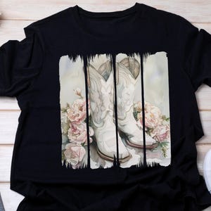 Pode incluir: Camiseta preta com um design de aquarela de botas de cowboy brancas e flores.