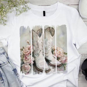Pode incluir: Camiseta branca com um design de aquarela de duas botas de cowboy brancas com flores cor-de-rosa.
