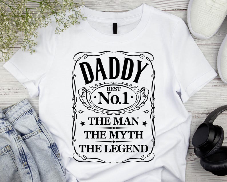 Pode incluir: T-shirt branca com um gr&aacute;fico preto que diz "DADDY BEST No.1 THE MAN THE MYTH THE LEGEND" em uma moldura decorativa. A camisa &eacute; feita de um material macio e &eacute; adequada para uso casual.