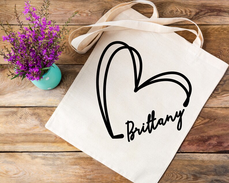 May include: A white canvas tote bag with a black hand-drawn heart and the name "Brittany" written underneath.