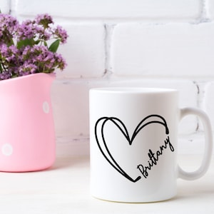 May include: White ceramic mug with a black outline of a heart and the name "Brittany" written inside the heart.