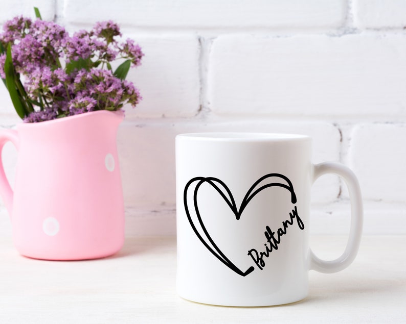 May include: White ceramic mug with a black outline of a heart and the name "Brittany" written inside the heart.