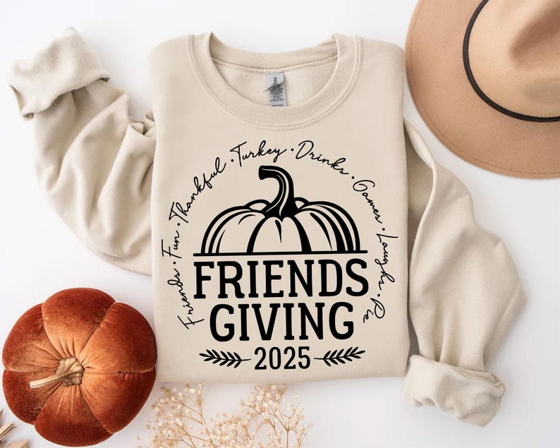 May include: A cream Friendsgiving sweatshirt featuring a black pumpkin design and the text "Friends Giving 2025". The design includes the words "Thankful, Turkey, Drinks, Games, Laughs, Pie, Fun" around the pumpkin.