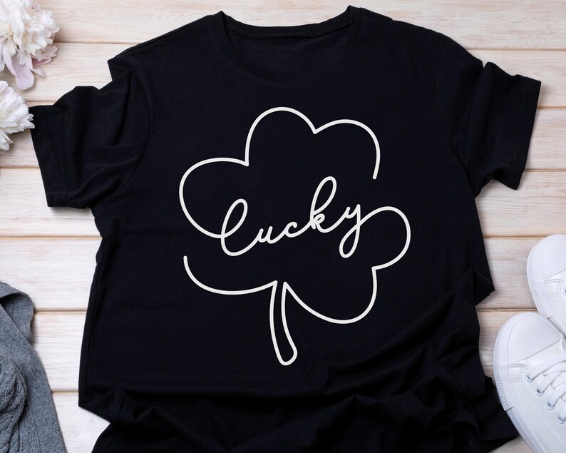 May include: Black t-shirt with a white outline of a four-leaf clover and the word "lucky" written inside.