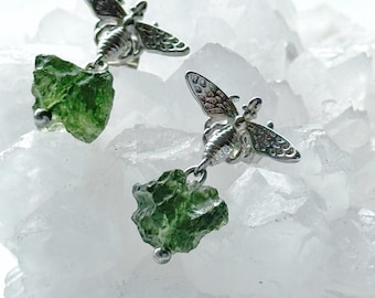 May include: A pair of silver bee earrings with green gemstone accents. The earrings are dangling and feature a detailed bee design.