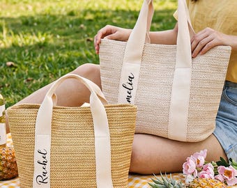 May include: Two woven straw tote bags with cream-colored handles and name tags. One bag says "Rachel" and the other says "Amelia". The bags are on a yellow and white checkered picnic blanket with fruit, drinks, and flowers.