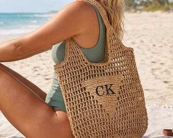 May include: A tan crochet tote bag with the letters "CK" in black. The bag is open at the top and has a rectangular pocket with the letters "CK" on the front. The bag is on a beach with sunglasses and a bottle of coconut water.