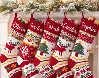 May include: Five knitted Christmas stockings hanging in a row, each featuring a red cuff with white embroidered names: Olivia, Amelia, Sarah, Cecilia, and Sophia. The stockings display festive patterns of reindeer, pine trees, and snowflakes.
