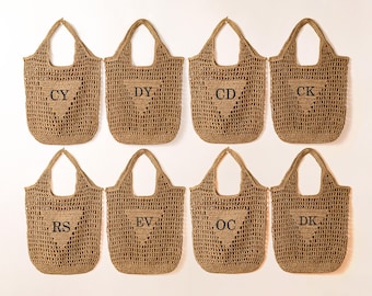 May include: Eight woven tote bags in a natural tan color are displayed. Each bag has a triangular pocket with two black letters: CY, DY, CD, CK, RS, EV, OC, and DK. The bags have a large handle.