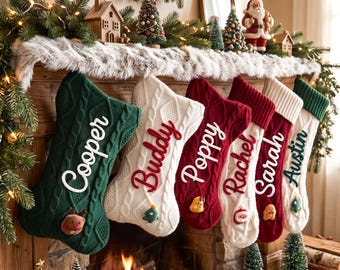 May include: A row of six cable-knit Christmas stockings hanging from a wooden mantel. The stockings are in dark green, white, and red, each featuring a personalized name in script embroidery and a small festive felt applique at the bottom.