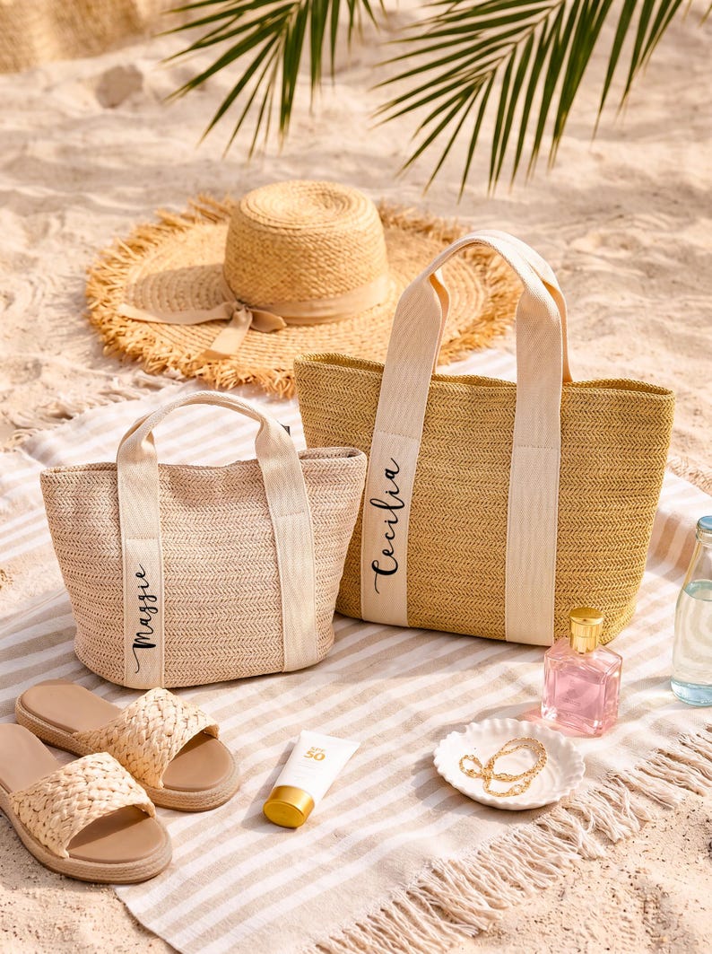 May include: Two woven straw tote bags with cream-colored handles and the names "Maggie" and "Cecilia" printed on them. A straw sun hat, sandals, sunscreen, perfume, and jewelry are also on a striped beach towel.