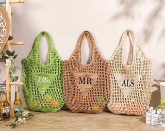 May include: Three open-weave crochet tote bags in green, tan, and cream. Each bag has a heart-shaped design and a personalized monogram. The green bag has "Ella" embroidered on it, the tan bag has "MR", and the cream bag has "ALS".