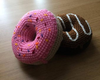 May include: Two crocheted doughnuts, one pink with colourful sprinkles and one brown with white icing.