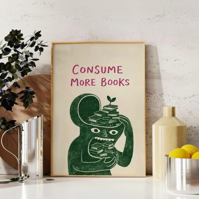 Puede incluir: Una impresi&oacute;n art&iacute;stica enmarcada con el texto "CONSUME MORE BOOKS" en rosa. La ilustraci&oacute;n presenta una figura verde con la cabeza abierta, llena de libros, y una peque&ntilde;a planta que crece en la parte superior. La figura sostiene y come libros.
